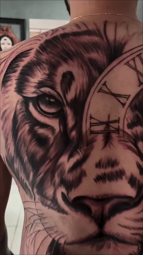 Close no leão com relógio de algarismos romanos tatuado nas costas