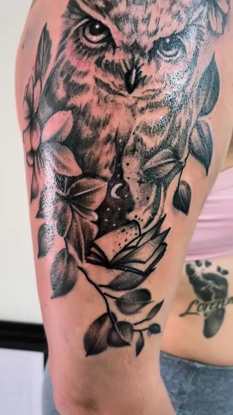Coruja entre folhas tatuada no braço, do ombro ao cotovelo